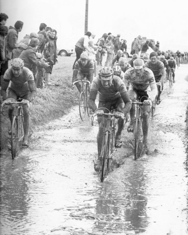 A bunch of cyclists led by Irish cycling legend Sean Kelly ride into a puddly during a very wet and muddy Paris-Roubaix in 1985